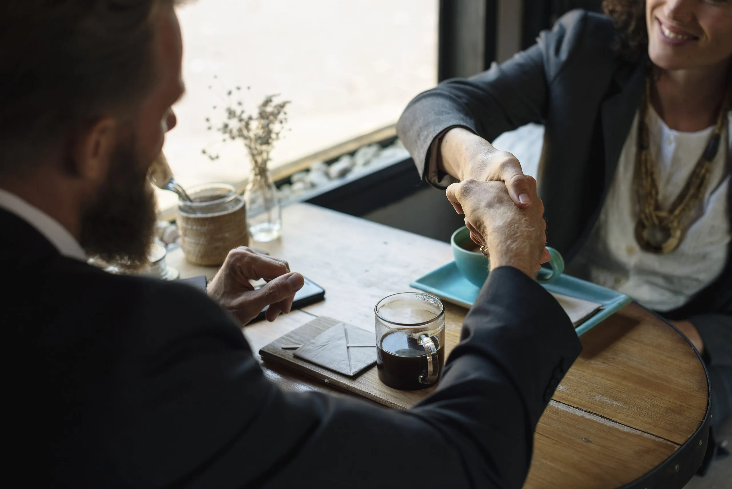 Two people shaking hands over a table at a coffee shop