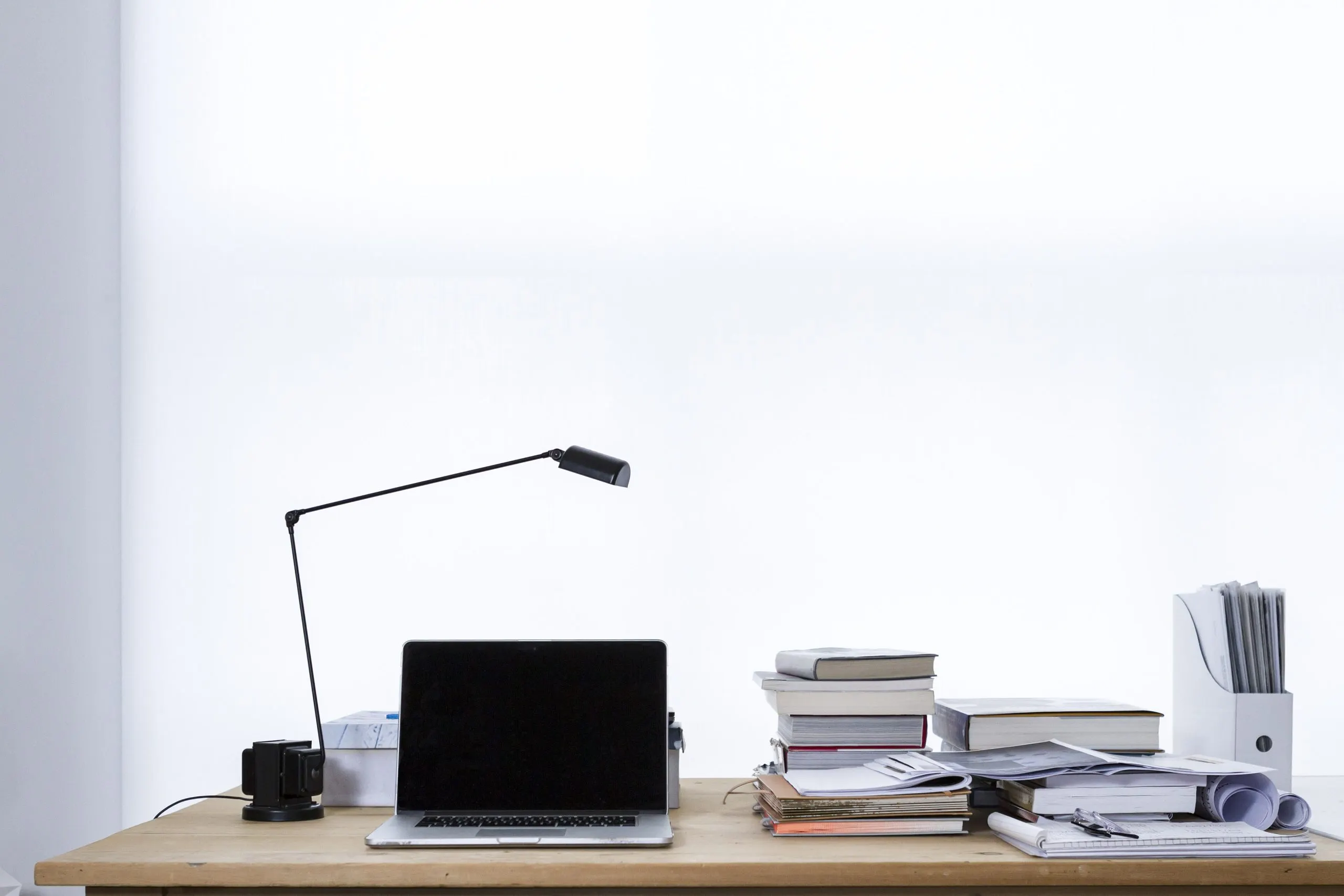 A laptop on a desk beside a stack of books